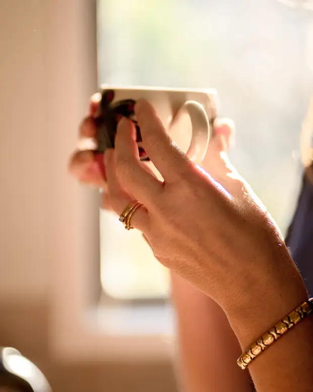 Hands holding a coffee mug by a sunlit window