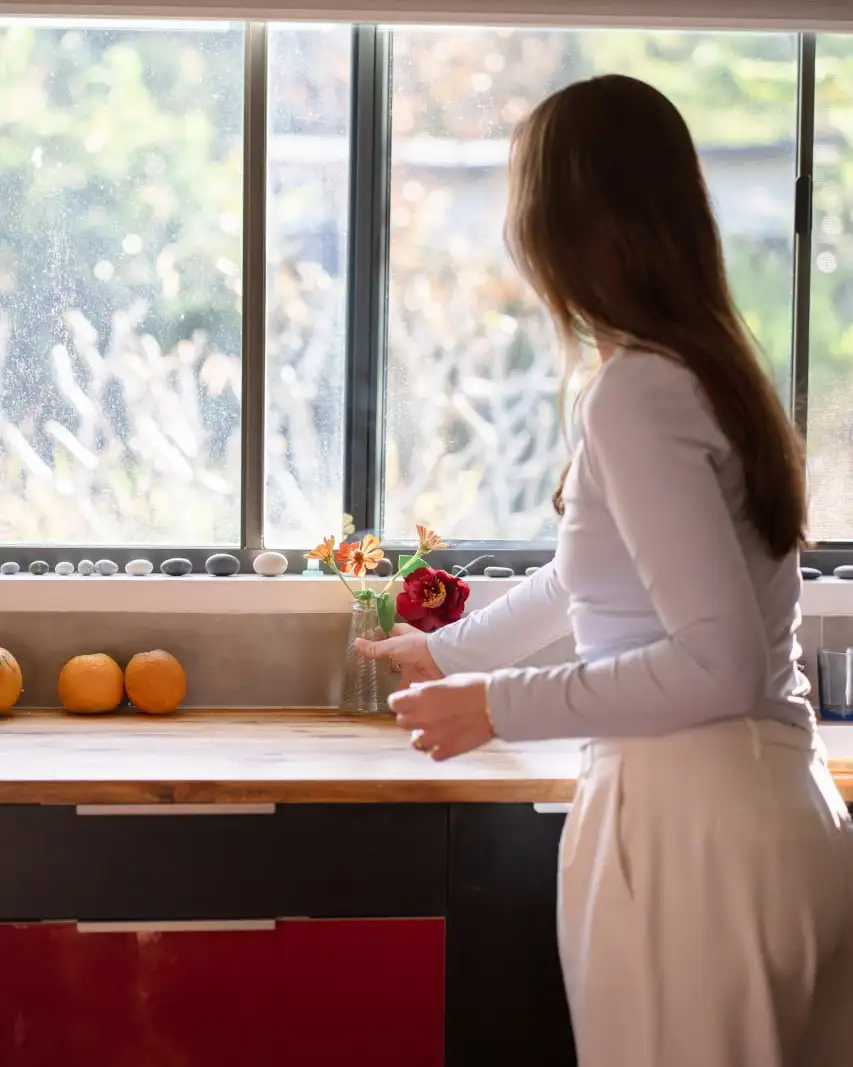 A woman arranging fresh flowers in a sunlit kitchen